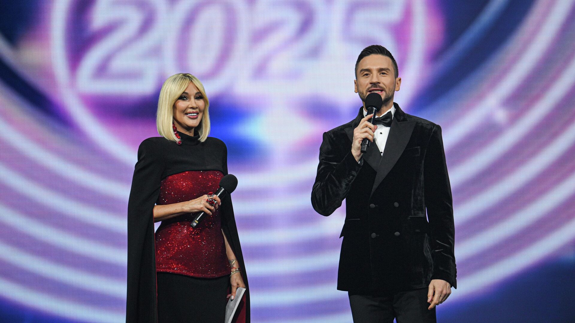 Ведущие Лера Кудрявцева и Сергей Лазарев выступают на концерте Песня Года 2025 в зале спортивного комплекса Мегаспорт в Москве