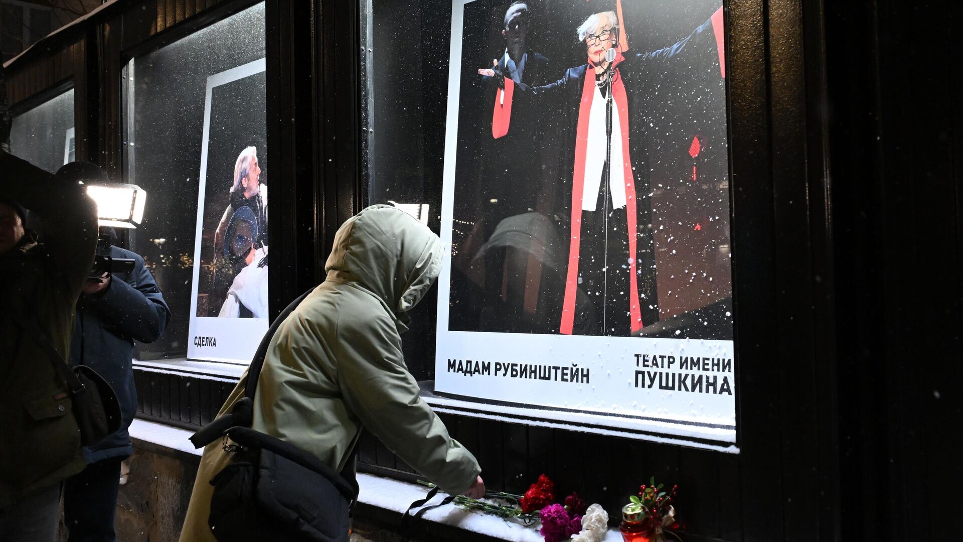 Женщина оставляет цветы у афиши спектакля Мадам Рубинштейн в Театре имени Пушкина